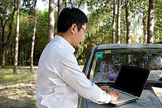 成功商务男士在汽车发动机盖上使用笔记本电脑