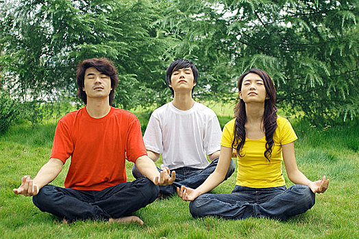 盘腿坐在草地上做瑜伽的三个年轻男女