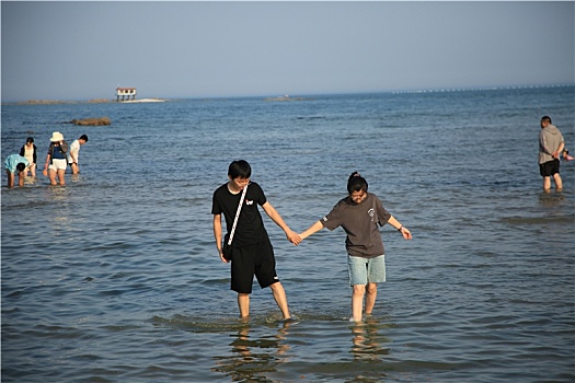 山东省日照市,海边旅游再掀高潮,游客赶海拾贝漫步沙滩感受清凉