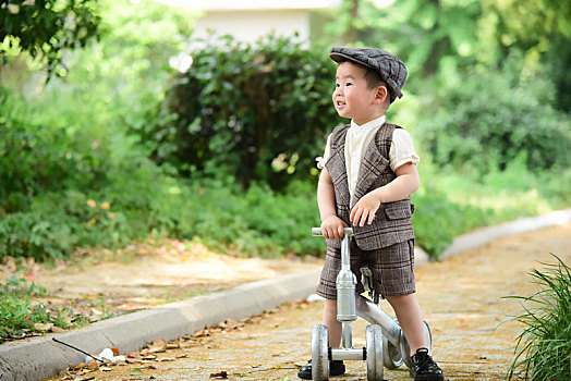 阳光下林荫小路上穿着短袖西服扶着滑滑车开心的小男孩