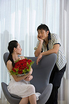 坐在椅子上捧着鲜花的女人与站在椅子后面的先生聊天