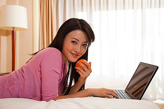 年轻女人趴在床上使用电脑