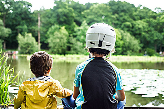 两个,孩子,兄弟,坐,水边,破旧,戴着,自行车头盔,后视图