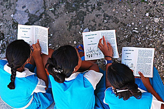 tuvalu,funafuti,elevated,view,of,schoolgirls,reading,book,while,sitting,on,graveled,ground