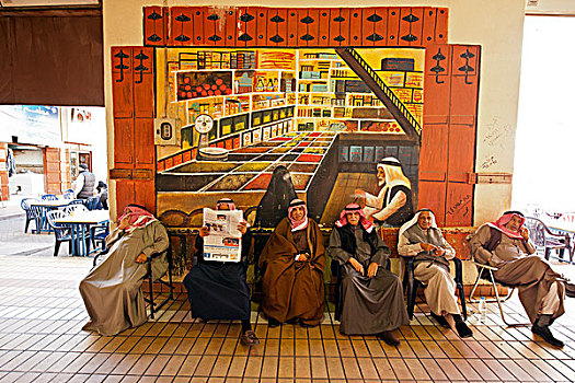 kuwait,city,senior,men,in,traditional,dress,sitting,and,reading,newspaper
