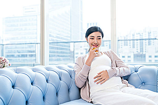 年轻孕妇坐在沙发上吃水果