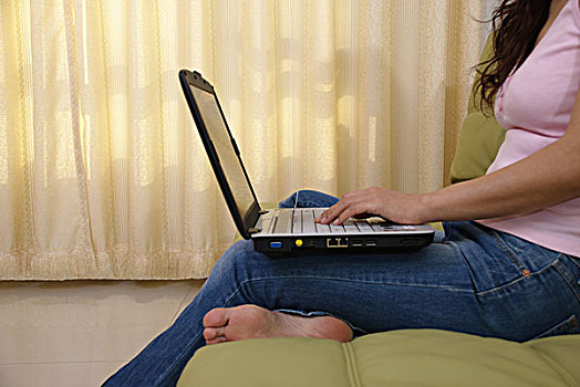 一名年轻女性坐在沙发上使用笔记本电脑