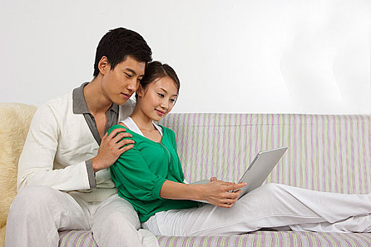 年轻情侣坐在沙发上使用笔记本电脑