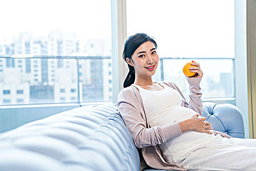 年轻孕妇坐在沙发上吃水果