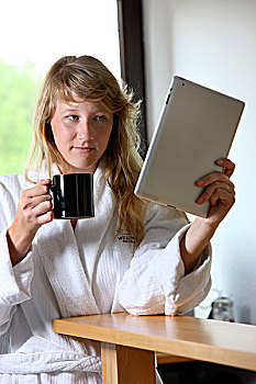 年轻,女人,穿,长袍,喝,杯子,咖啡,早晨,坐,厨房,读,上网,报纸,电脑