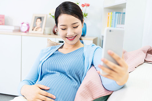 年轻孕妇在沙发上使用手机