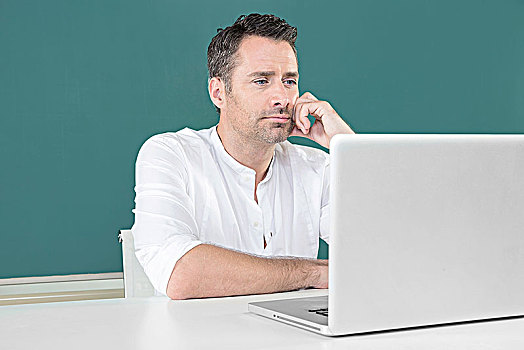 坐在黑板前看电脑的男士