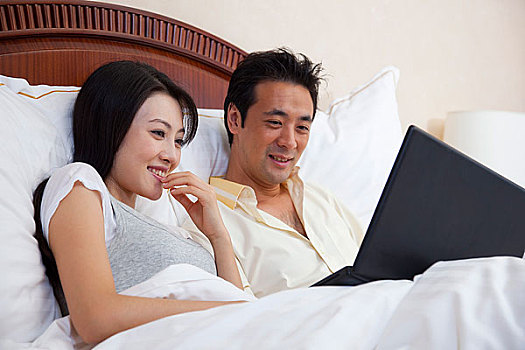 夫妻躺在床上使用电脑