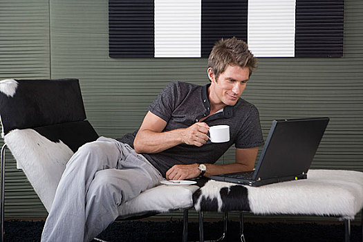 一位先生坐在躺椅上喝咖啡玩电脑