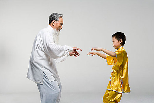 一位老者正在教一个小男孩练太极