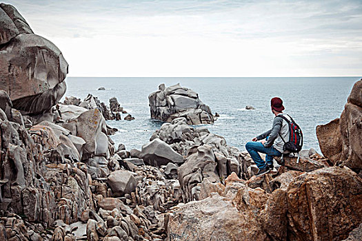后视图,男青年,坐,石头,观景,海洋,哥斯达黎加,萨丁尼亚,意大利