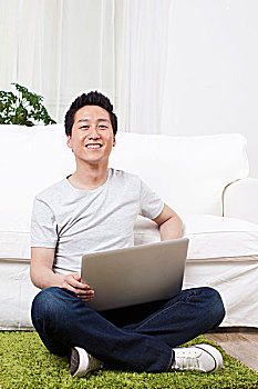 一个坐在绿色地毯上用笔记本电脑的青年男士