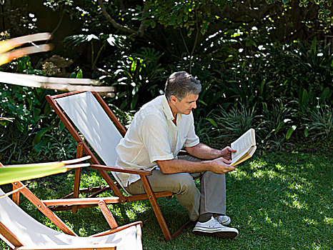 男人,坐,折叠躺椅,花园,读,书本