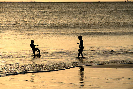 巴厘岛金巴兰海滩金色日落两小孩游戏剪影