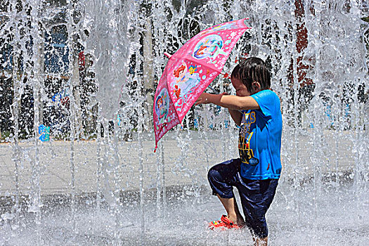 喷泉里撑伞玩水的女孩