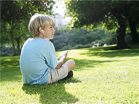 金发,男孩,7-9岁,坐,草,公园,听,mp3播放器,侧面视角