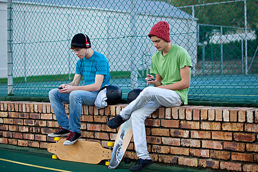 两个,青少年,男孩,坐,砖墙,滑板,听歌,手机