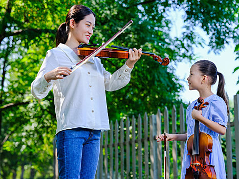 年轻女性在公园指导女孩拉小提琴