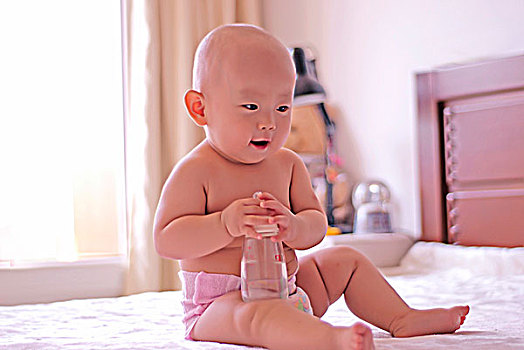 一名八个月的婴儿坐着玩奶瓶