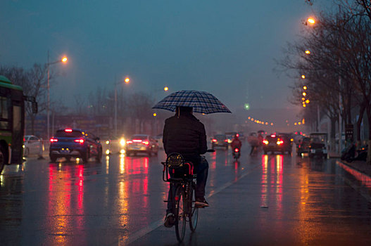 骑自行车撑伞的人走在夜晚城市道路上