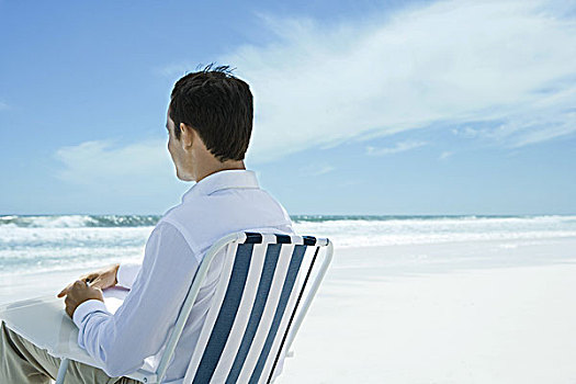 男人,坐,折叠椅,海滩,笔,纸,后视图