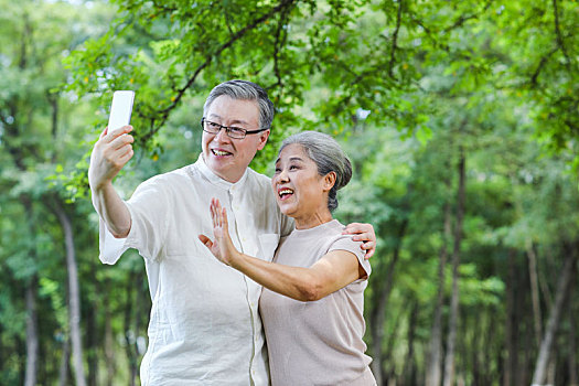 幸福的老年夫妇在公园使用手机自拍