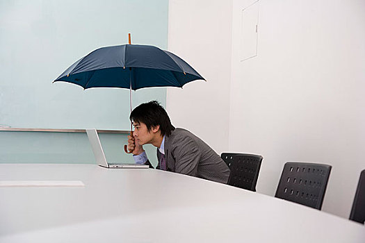 在会议室内打着伞工作的男员工