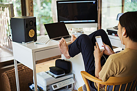 男人,坐,室内,书桌,电脑,抬腿,赤足,拿着,手机