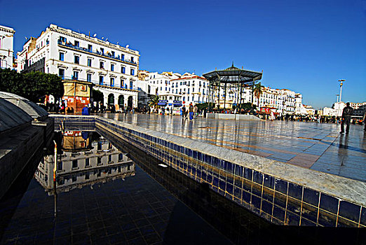 algeria,algiers,reflection,of,building,on,pool,with,people,walking,tiled,floor,in,background