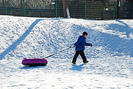 一个儿童拖着气垫走在雪地上
