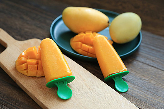 用芒果果泥制作的芒果雪糕和新鲜切好的芒果摆放在木桌上