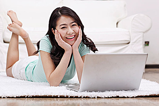 年轻女士趴在地毯上使用电脑