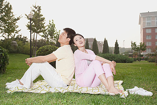 年轻情侣背靠背坐在草地上