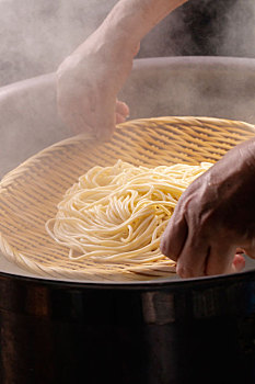 竹箕在大锅中捞起热腾腾的面,面条弹牙有食欲感