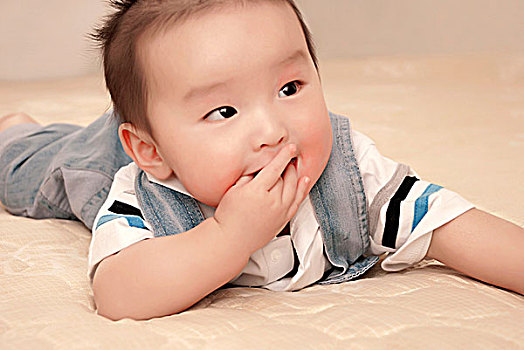 一名7个月大的男婴趴在床上吃手指