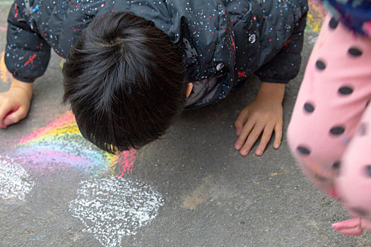 小孩在室外的公园地板上,用粉笔快乐的涂鸦画画