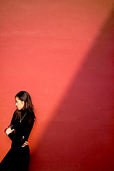 穿着一身黑的女人靠在红墙上