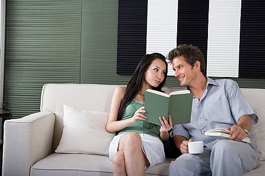 一对年轻夫妻坐在沙发上看书聊天