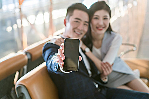 年轻情侣在候机室展示手机