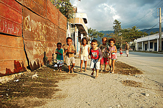 east-timor,timor-leste,dili,group,of,timorese,children,running,in,the,street,under,dark,clouds,with,a,blond,boy,middle,thumbs,up