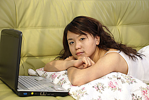 一名年轻女性趴在在沙发上使用笔记本电脑