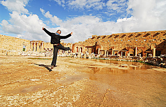 libya,leptis,magna,woman,jumping,in,the,air,with,ruins,background,unesco,world,heritage,site