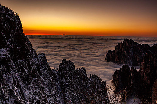 中国安徽黄山风景区,冬日雪后放晴,夕阳映照山崖云雾飘渺宛若仙境