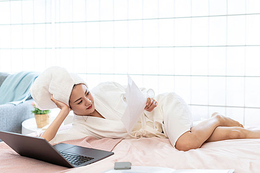 年轻女子穿着浴袍在床上使用电脑