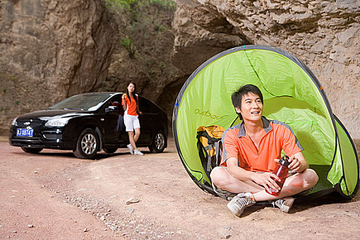 一对年轻人开着奥迪车在郊外的山洞前的帐蓬边休息